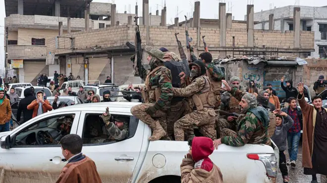 Suriye'nin kuzeyinde orduya bağlı güçler bir arazi aracının üstünde silahlarıyla görülüyor. Etraftaki siviller telefonlarıyla video çekiyor.