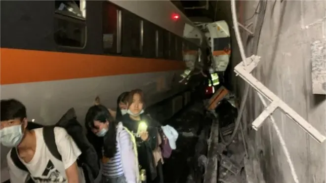 People walk next to a train which derailed in a tunnel north of Hualien