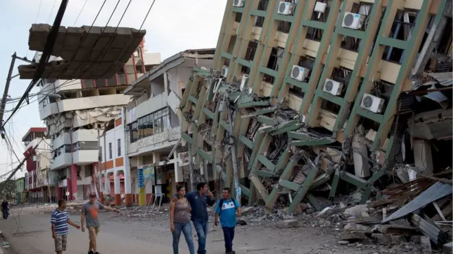 Residents walk past a row of collapsed buildings felled by the 7.8-magnitude earthquake, in Portoviejo, Ecuador, Monday, April 18, 2016