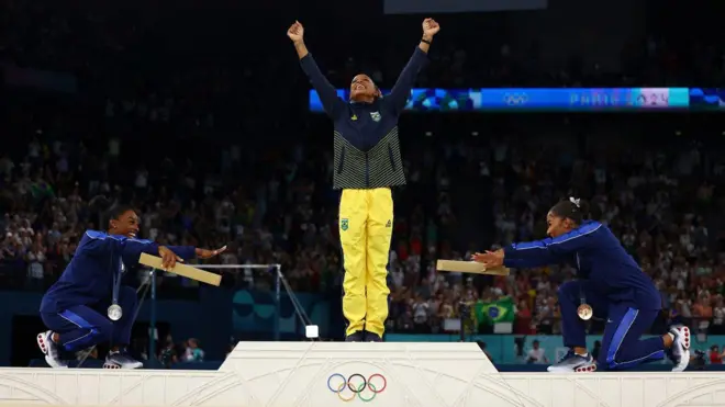 Rebeca está no pódio com Simone Biles e Jordan Chiles, que se curvam em reverência à atleta brasileira 