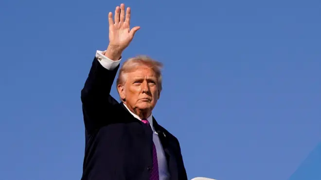 Трамп машет рукой на фоне голубого неба