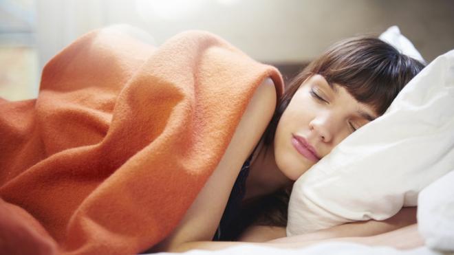 Mujer durmiendo sobre almohada y cubierta con un manto naranja