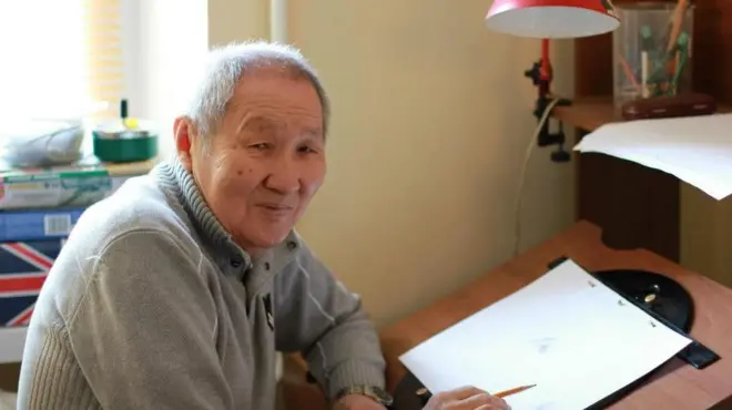 Радна Сахалтуєв на схилі літ схилився за робочим місцем і малює щось на аркуші