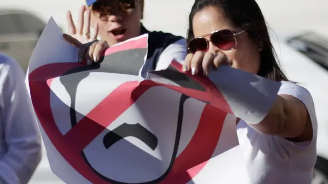 A Venezuelan in Honduras rips a sign depicting Nicolas Maduro