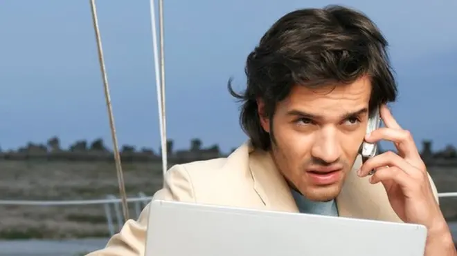 Un hombre que trabaja en su laptop entre cuerdas de navegación (de vacaciones)