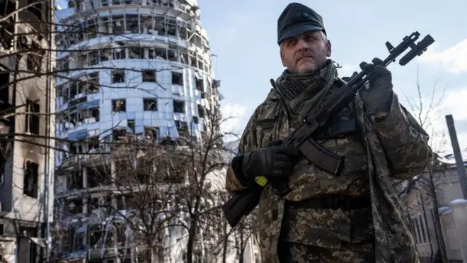 Umusirikare uhagaze imbere y'inyubako yangijwe na misile zayirashweho muri Kharkiv