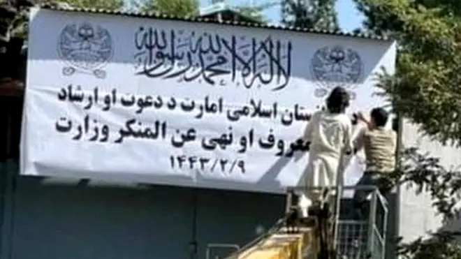 People on a mechanical crane attend to a white signboard outside a building in Kabul