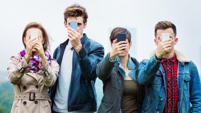 Cuatro jóvenes con los rostros tapados por sus teléfonos celulares, una imagen que busca crear la idea de la adicción a las redes