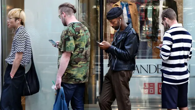 四个男人排成一队，看着自己的智慧型手机。