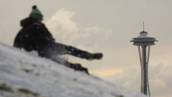 Someone sledges down a hill with the Seattle Space Needle visible in background