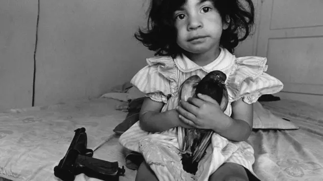 Durante los últimos 30 años, Donna de Cesare ha estado documentando los efectos de la guerra y la violencia de las bandas de jóvenes en América Central y las comunidades de refugiados en los EE.UU. Una niña de tres años sostiene una paloma llamada Esperanza. Su tío ya no puede caminar después de un ataque de pandillas en Watts, Los Ángeles.