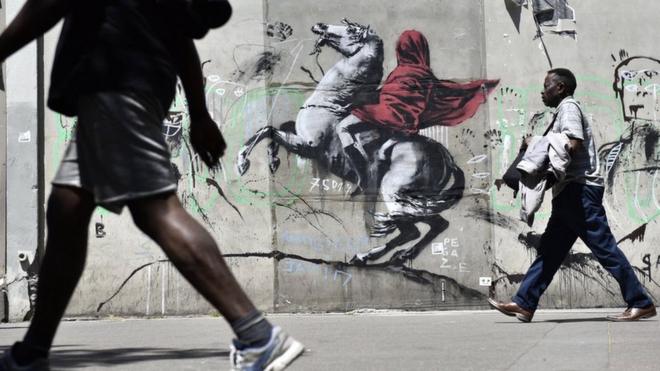 People walk by a recent artwork believed to be attributed to Banksy showing Napoleon rearing his horse, wrapped in a red cloak in the 19th district of Paris