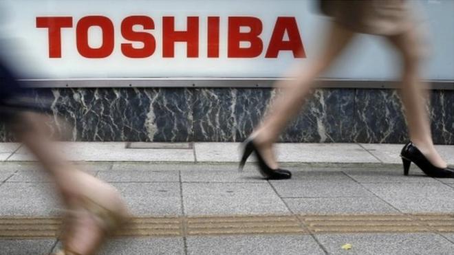 Pedestrians walk past a logo of Toshiba Corp outside an electronics retailer in Tokyo.