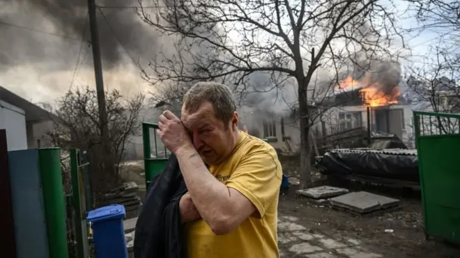 Ukraine man crying in front of a burning building