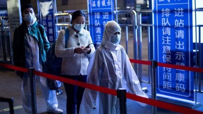 Passengers wear hazmat suits as they arrive at the Wuhan Wuchang Railway Station in Wuhan, to leave the city early on April 8, 2020.