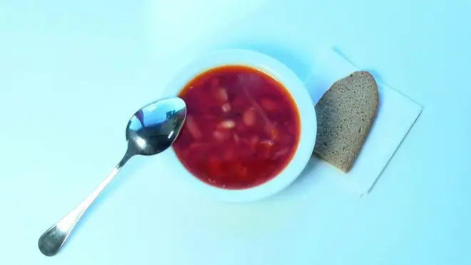 Миска борщу зі скибкою хліба.