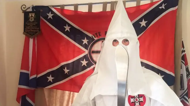 Thomas segura um facão vestido com o traje característico da Ku Klux Klan