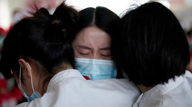 Tiga pekerja medis berangkulan di Bandara Internasional Wuhan Tianhe setelah lockdown di Kota Wuhan dicabut pada 8 April 2020.