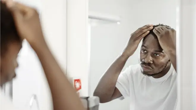 Un homme vérifie sa chevelure devant un miroir