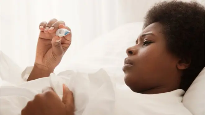 Une femme couchée sur un lit qui lit un thermomètre