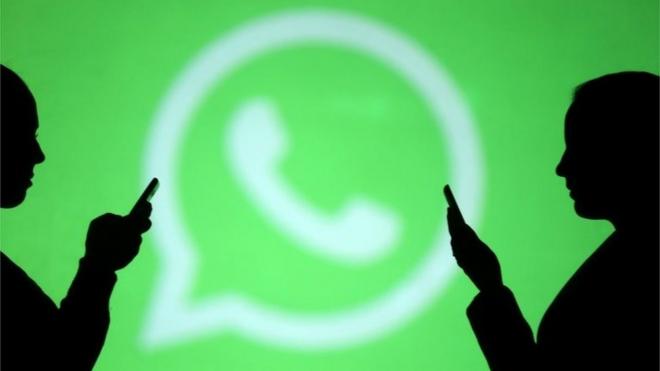 Pessoas usam celular com logo do WhatsApp ao fundo