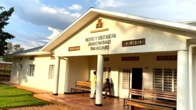 Ifoto mbarankuru igaragaza inyubako y'urukiko rw'ibanze rwa Kicukiro. Imbere ku ibaraza hicaye umuntu utaboneka neza mu maso uri ku ntebe ndende, mu gihe imbere ye hahagaze undi muntu.