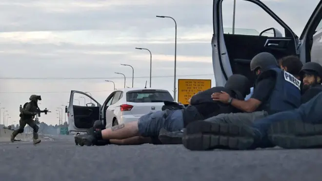Journalists take cover behind cars as Israeli soldiers take position during clashes with Palestinian fighters near the Gevim Kibbutz, close to the border with Gaza on 7 October, 2023
