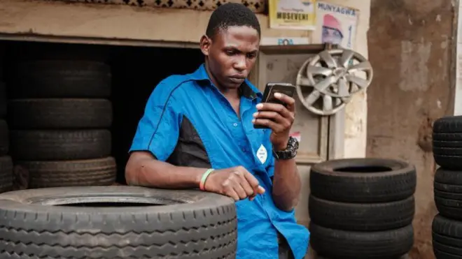 Umugabo wambaye ishati y'ubururu, uhugiye muri telefoni igendanwa