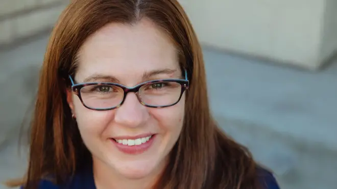 Ellie Leonard sonríe a la cámara. Lleva gafas.   