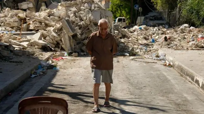 رجل لبناني مسن يسير أمام مبنى دمره هجوم جوي إسرائيلي مؤخراً