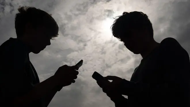 صورة لخيال طفليين لاتبدو ملامحهما يقفان وجها لوجه وكل منهما يتصفحه هاتفه النقال