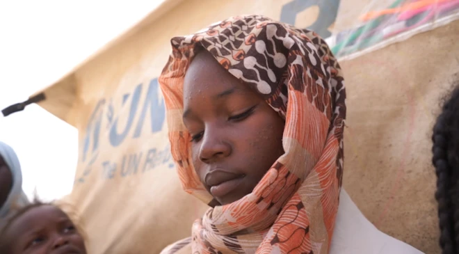 تُظهر الصورة صفاء، الفتاة السودانية البالغة من العمر 14 عاماً، وهي تجلس في مخيم للاجئين مع خمسة أطفال آخرين. 