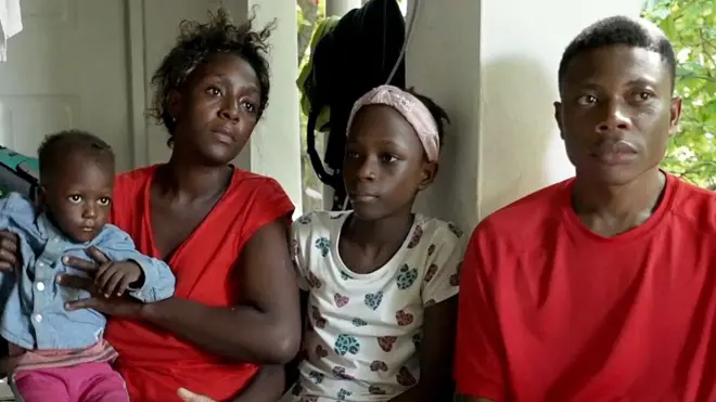 Une famille composée de deux adultes, d'un enfant et d'un bébé détourne le regard de la caméra alors qu'elle est assise à la maison, lors d'une interview pour le reportage.