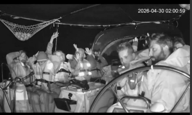 Siyah beyaz görüntüde, ellerini havaya kaldırmış kişileri teknenin güvertesinde görüyoruz.