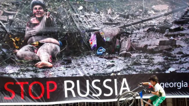 Мальчик с велосипедом перед плакатом «Stop Russia» в Тбилиси