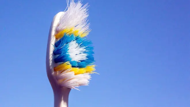 Close up of tooth brush with yellow, blue and white bristles with white background