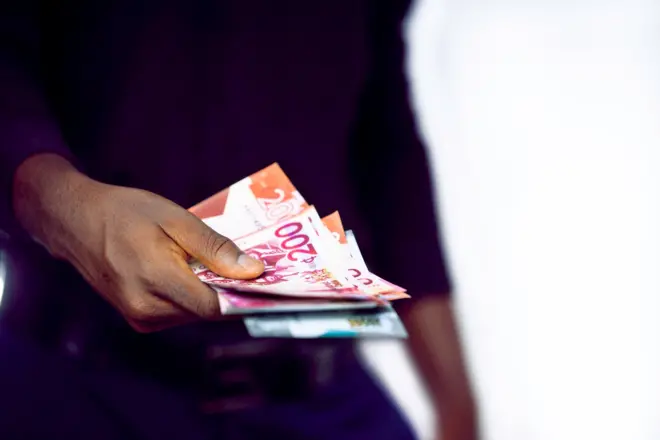 Umugabo yambaye ishati yirabura y'amaboko maremare afise mu minwe inoti z'amafaranga y'ama 'cedi' yo muri Ghana.