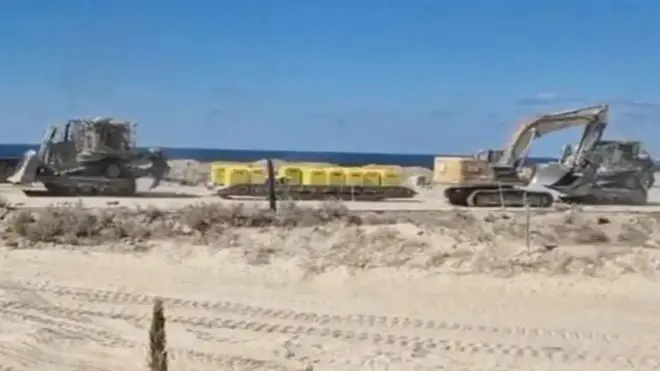 چند لودر در حال نصب موانع زرد رنگ در یک مسیر شن و ماسه‌