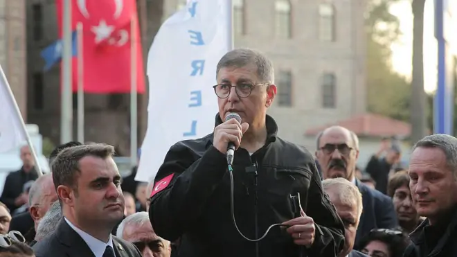 Cemil Tugay bir etkinlikte elinde mikrofonla konuşurken