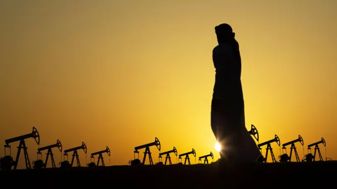 La silueta de un hombre árabe observa decenas de unidades de bombeo de petróleo contra la puesta del Sol