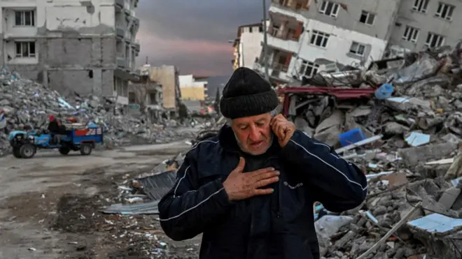 A man makes a phone call with destroyed buildings behind him