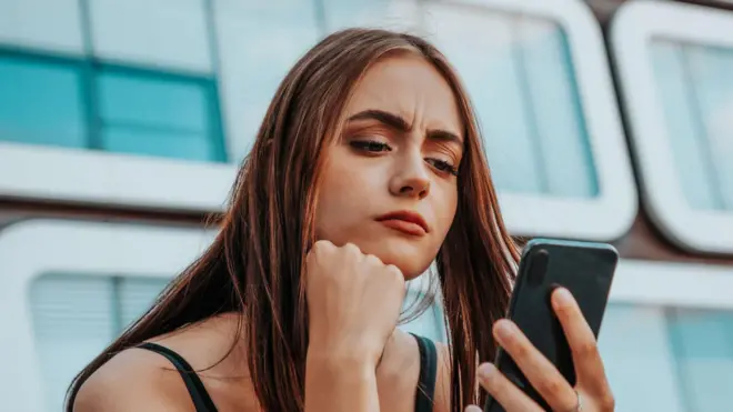 एक युवा महिला चिंतित होकर अपने स्मार्टफोन को देख रही है