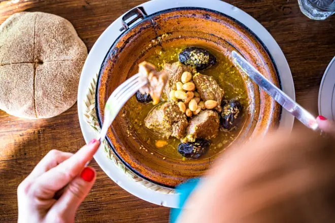 طبق من حساء اللحم بالبرقوق وسيدة تظهر أصابعها وهي تأكل منه بأدوات المنضدة