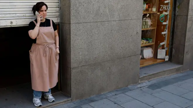 A woman stands beside a dark doorway of a closed shop in Spain