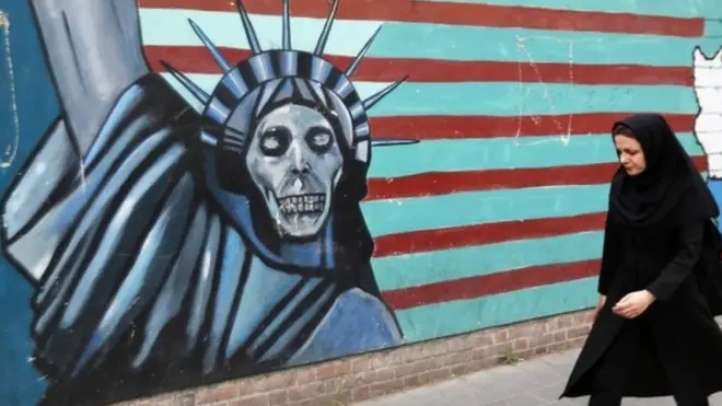 Женщина в Тегеране на фоне изображения, нарисованного на стене здания, где располагалось посольство США в Иране.