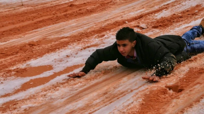 Joven se desliza en la nieve del desierto del Sahara.