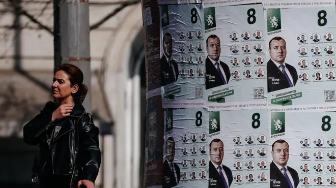 Женщина в Софии идет мимо расклеенных предвыборных плакатов в апреле 2026 года