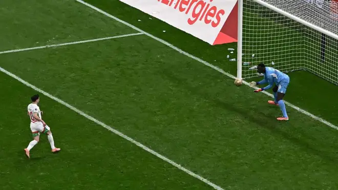 Futbolcu penaltıyı yeni kullanmış top havada gidiyor, Kaleci olduğu yerde topun kucağına gelmesini bekliyor.