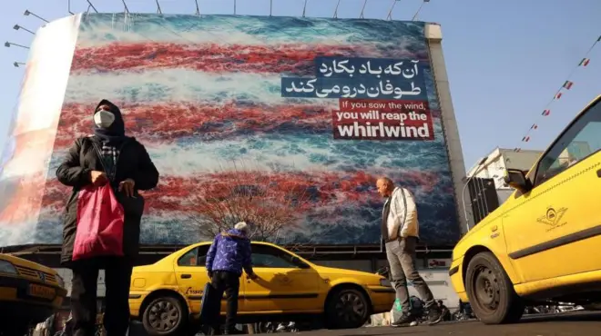 Fotoğrafın ön planında bir kadın alışveriş çantası taşırken, bir adam sarı bir taksiye biniyor. Arka planda ise “Rüzgâr eksen, fırtına biçersin” yazan devasa bir ABD karşıtı reklam panosu görünüyor. 