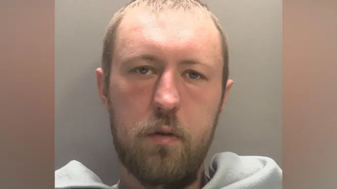 A mug shot of John Ashby who has short light brown hair and facial hair. he has a grey blanket across his front